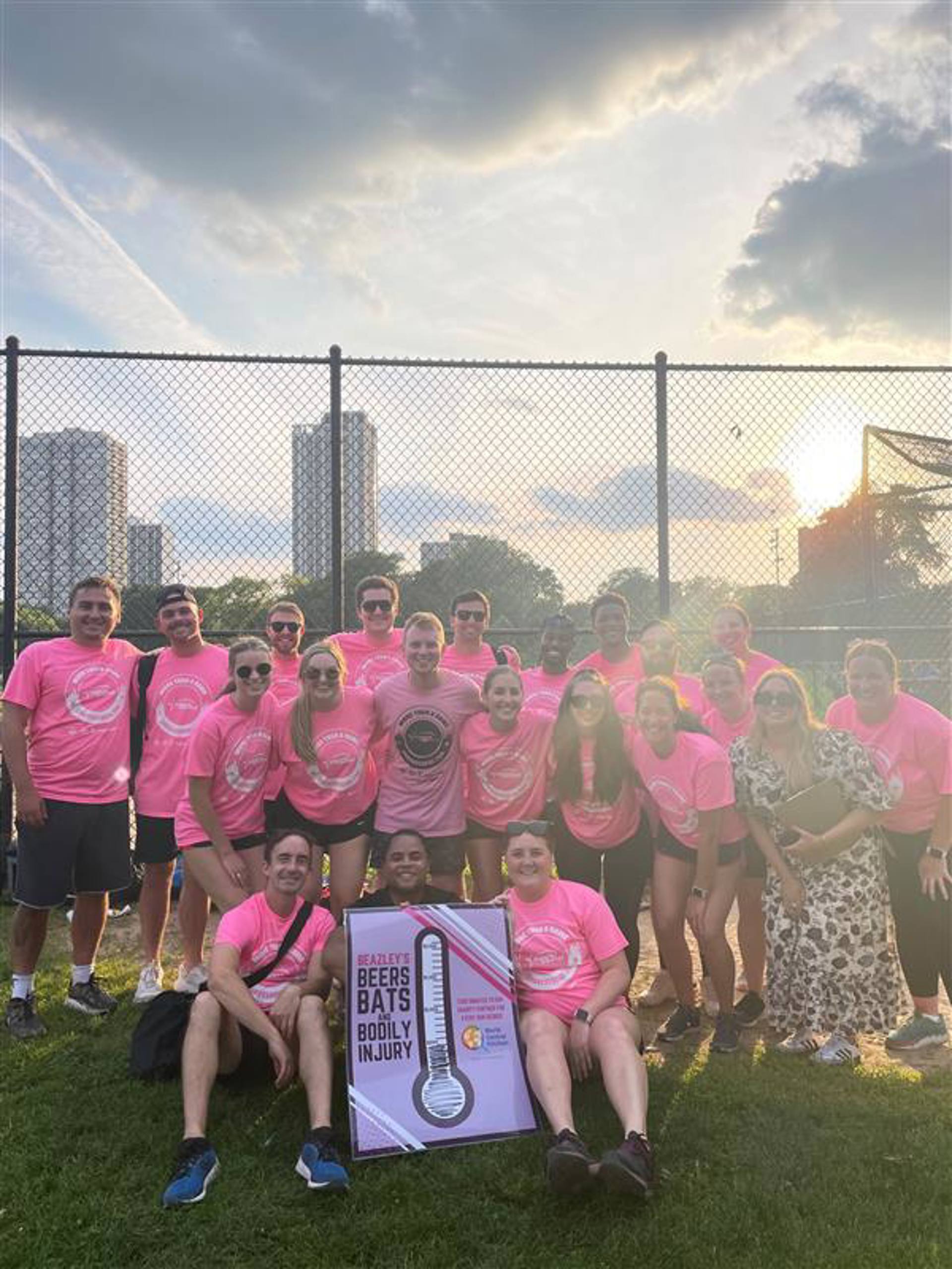 A group of individuals wearing pink shirts smiles and poses together for a photograph.